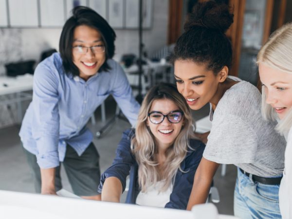 Close-up portrait of freelance it-specialists looking at laptop screen with smile. Asian programmer in glasses helping to mulatto girl in white t-shirt with her project.